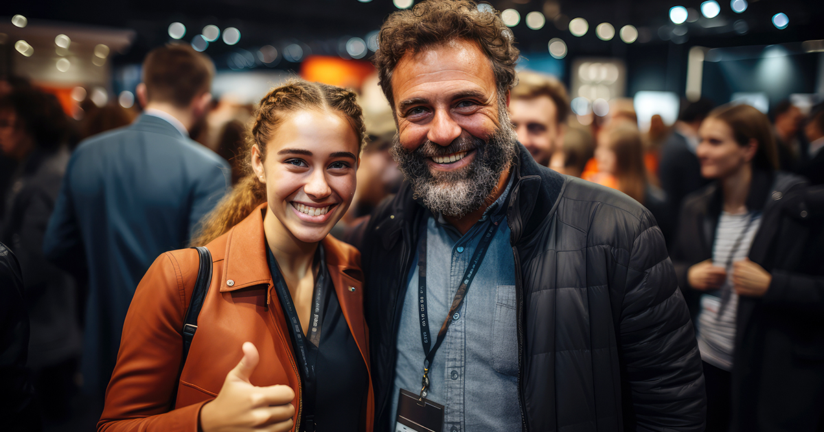 Happy exhibition attendees on show floor, female and male, with female giving a thumbs up